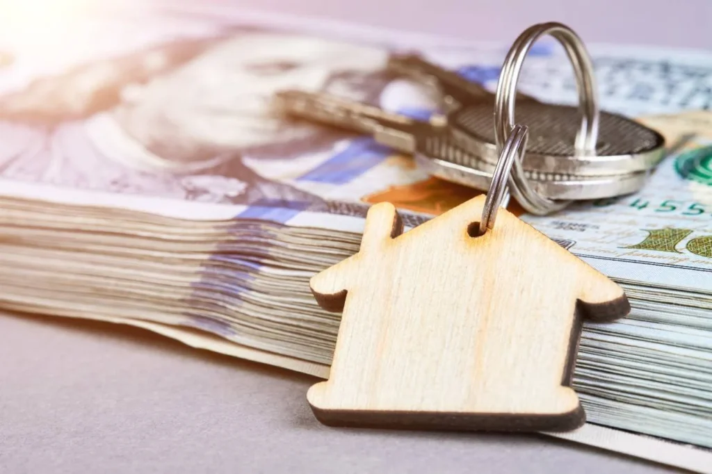 trousseau de clé avec un porte clé en forme de maison posé sur une liasse de billets